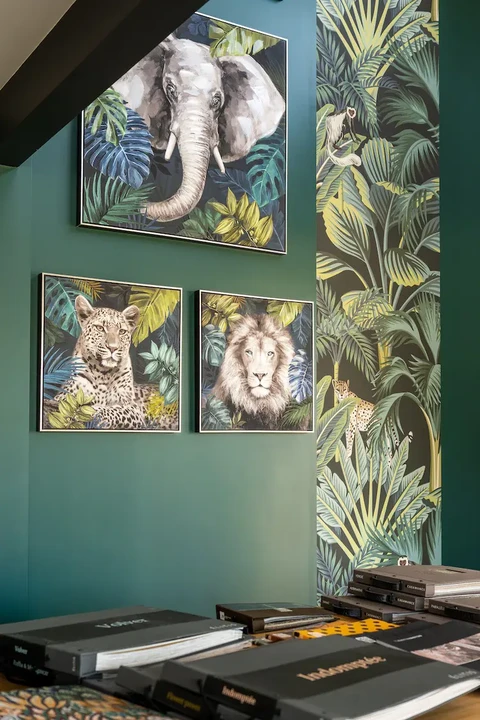 Intérieur moderne avec mur vert émeraude décoré de trois tableaux encadrés représentant des animaux sauvages (éléphant, léopard, lion) dans un style jungle tropicale