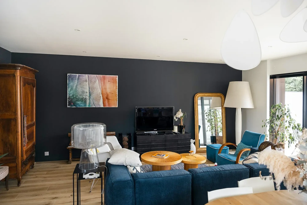 Salon moderne avec mur accent bleu foncé, canapé bleu marine, fauteuils en cuir bleu, tables basses rondes en bois