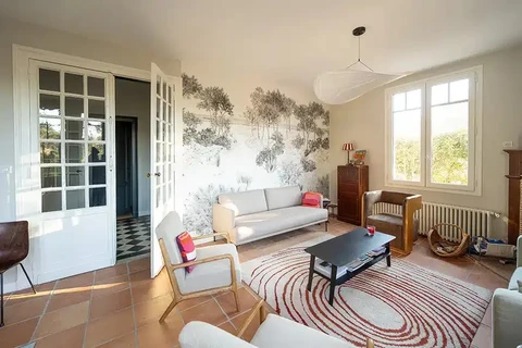 Salon lumineux avec canapé gris clair, fauteuil moderne et table basse noire sur tapis rayé rouge et blanc