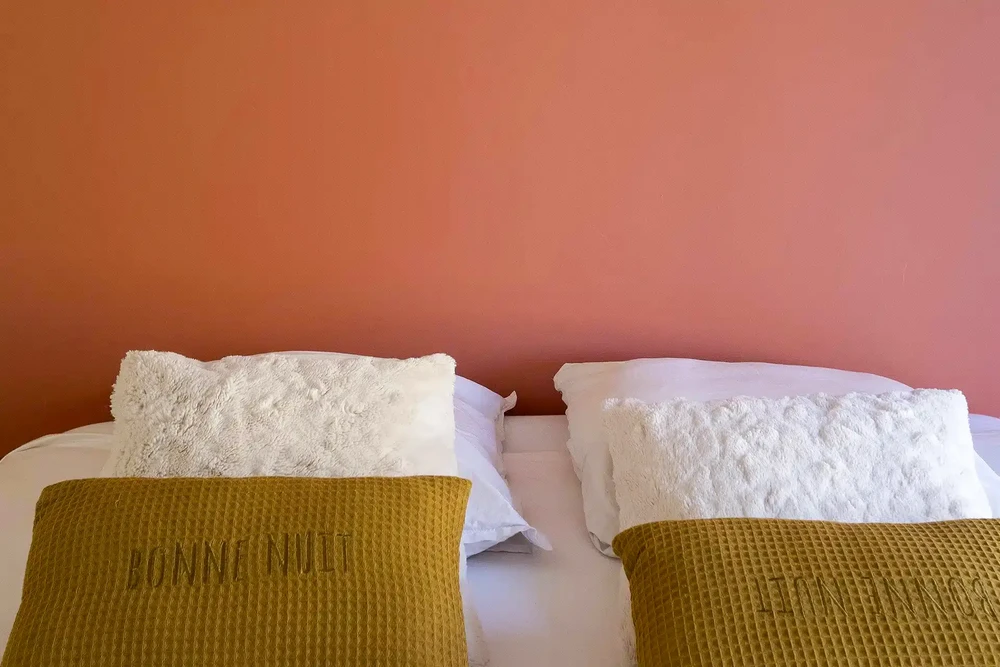 Chambre d'hôtel avec deux oreillers blancs texturés disposés sur literie blanche, rehaussés de plaids moutarde tricotés