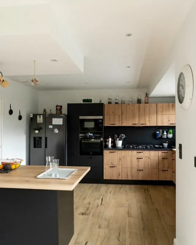 Salon lumineux avec canapé gris clair, fauteuil moderne et table basse noire sur tapis rayé rouge et blanc