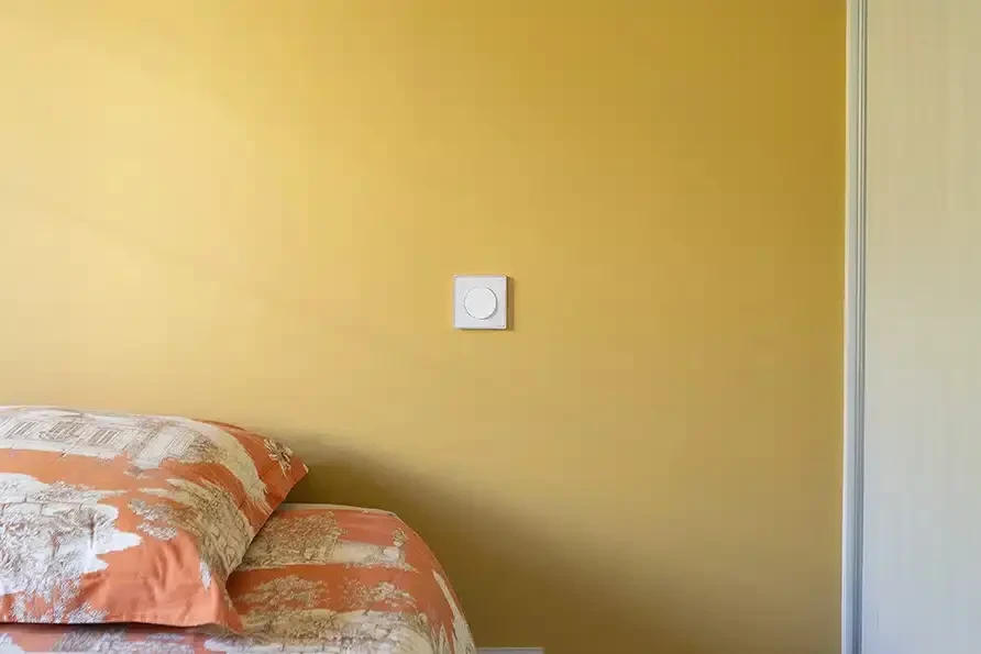 Salon moderne avec canapé d'angle gris clair, coussins bleu marine et turquoise, poutres apparentes peintes, suspensions en rotin tressé, parquet chêne massif à lames larges, mur accent avec fresque murale abstraite rose et grise, éclairage LED intégré, mobilier contemporain sur pieds métalliques noirs